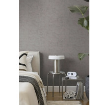 Grijs vliesbehang met betonlook in moderne slaapkamer met bed, zilveren kruk, lamp en grote kamerplant.