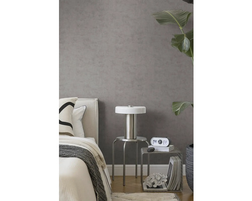 Grijs vliesbehang met betonlook in moderne slaapkamer met bed, zilveren kruk, lamp en grote kamerplant.