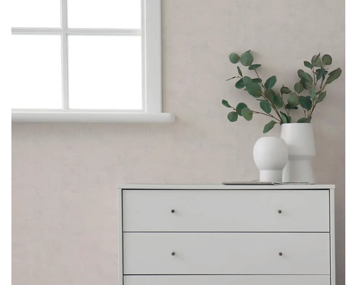 Lichte kamer met witte ladekast, eucalyptus takken in witte vazen en raam voor een muur met textuur.