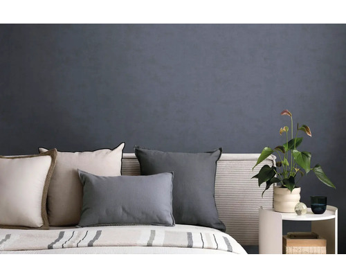 Slaapkamer met donkergrijs gestructureerd behang, bed met diverse kussens en een bijzettafel met een kamerplant.