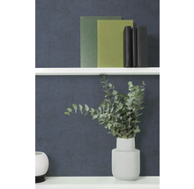 Gestructureerd effen behang in donkerblauw achter een witte wandplank met boeken en een vaas met eucalyptustakken.