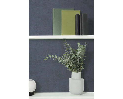 Gestructureerd effen behang in donkerblauw achter een witte wandplank met boeken en een vaas met eucalyptustakken.