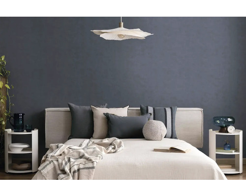 Moderne slaapkamer met bed, diverse kussens, een hanglamp en nachtkastjes voor een muur met textuur.