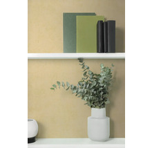 Getextureerd okergeel behang in een modern interieur met witte planken, boeken en een vaas met eucalyptus.