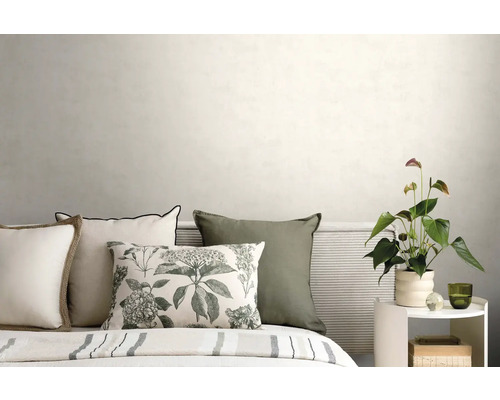 Bed met sierkussens, geribbeld hoofdbord en witte bijzettafel met plant voor een lichte muur in een moderne slaapkamer.