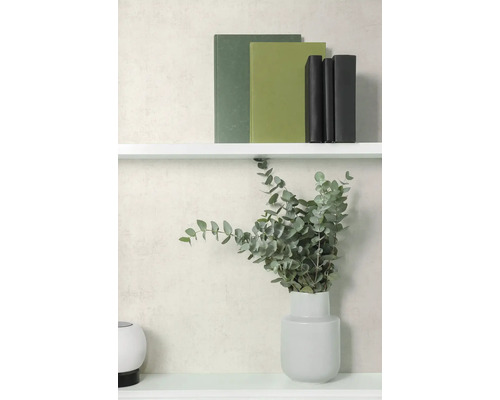 Vliesbehang met subtiele structuur in lichtbeige achter een witte plank met boeken en een vaas met eucalyptus takken.