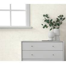 Licht gestructureerd behang op een muur achter een grijze ladekast met vazen en eucalyptus takken naast een raam.