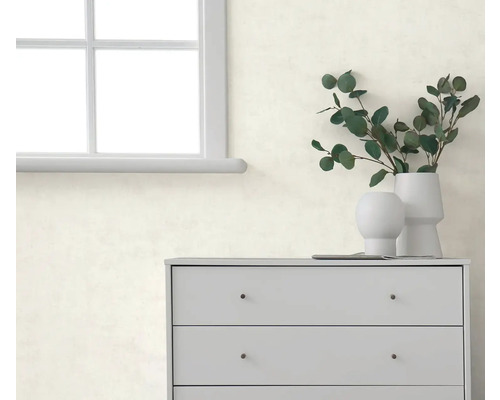 Licht gestructureerd behang op een muur achter een grijze ladekast met vazen en eucalyptus takken naast een raam.