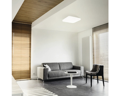 Woonkamer met bank, stoel, jaloezieën en plafondlamp