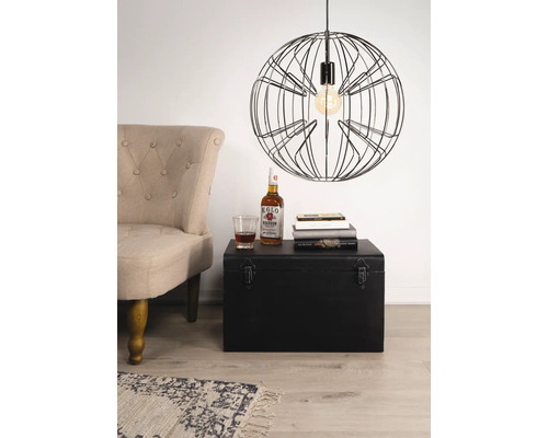 Scène met een fauteuil, een zwarte kist, boeken, een drankje en een hanglamp met draadframe.