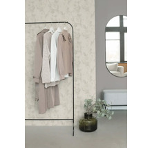 Licht ingerichte, georganiseerde kamer met vliesbehang met bloemmotief, metalen kledingrek, ovale wandspiegel en een bankje.