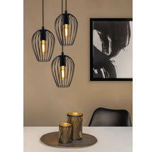 Drie zwarte hanglampen met draadlampenkappen boven een eettafel met decoratie