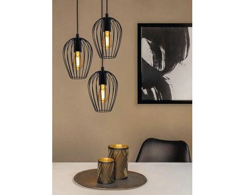 Drie zwarte hanglampen met draadlampenkappen boven een eettafel met decoratie