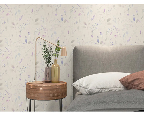 Vliesbehang met fijn bloemenpatroon in een lichte slaapkamer met grijs gestoffeerd bed en houten nachtkastje.