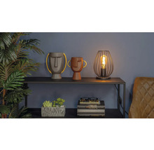 Decoratieve scène met twee vazen met gezichten, een lamp en een stapel boeken op een plank.