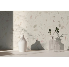 Licht behang met verfijnd bloemenpatroon en grassen, met daarvoor een witte keramieken vaas en twee glazen vazen op een licht oppervlak.