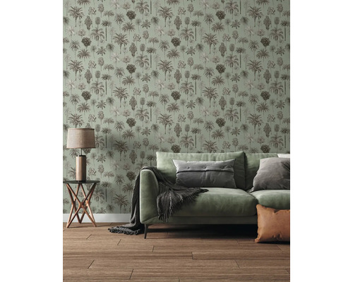Vliesbehang met palmenpatroon in een lichte woonkamer met groene bank en houten vloer.