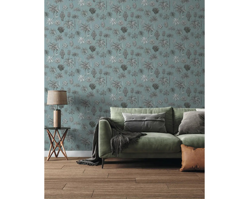 Woonkamer met behang met palmboompatroon, groene bank met kussens en deken, houten bijzettafeltje met lamp en houten vloer.