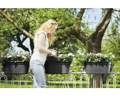 Vrouw verzorgt bloemen in balkonbakken op een balkonreling