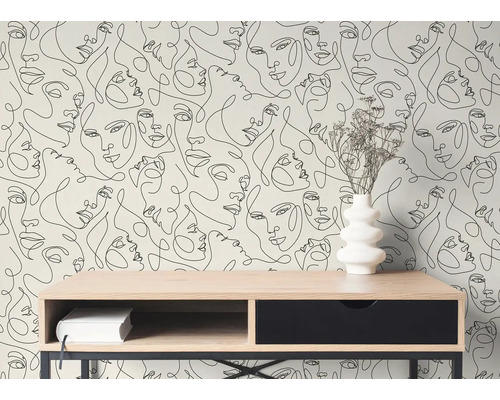 Modern behang met zwarte lijntekeningen van gezichten achter een houten bureau met een witte vaas en droogbloemen in een lichte kamer.