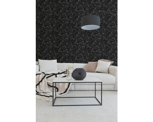 Woonkamer met zwart behang met witte gezichten in lijntekening, een lichte corduroy bank en een witte salontafel met een zwart metalen frame.