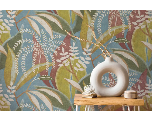 Vliesbehang met groot bladpatroon in blauw, groen en bruin achter houten sidetable met ronde witte vaas.