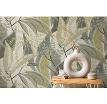 Vliesbehang met groot bladerpatroon achter een houten tafel met witte ronde vaas en decoratie.