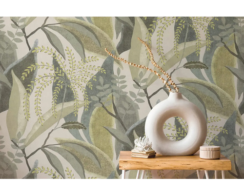 Vliesbehang met groot bladerpatroon achter een houten tafel met witte ronde vaas en decoratie.