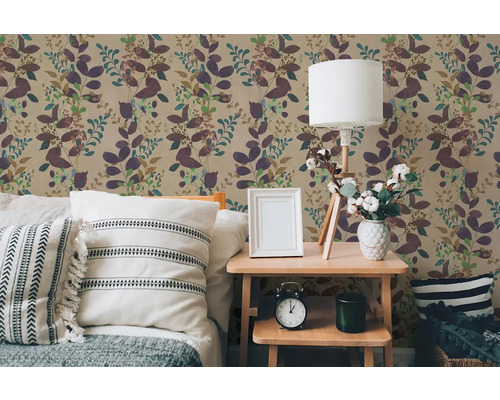 Vliesbehang met floraal bladerpatroon in een slaapkamer met een licht houten nachtkastje en kussens.
