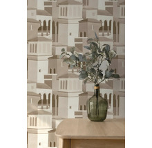 Vliesbehang met architectuurpatroon van een mediterrane stad, met daarvoor een houten tafel met een glazen vaas en groene takken.