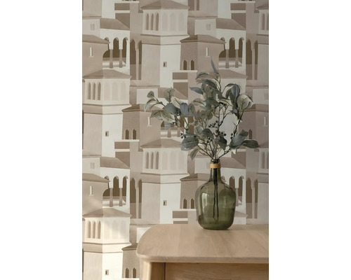 Vliesbehang met architectuurpatroon van een mediterrane stad, met daarvoor een houten tafel met een glazen vaas en groene takken.