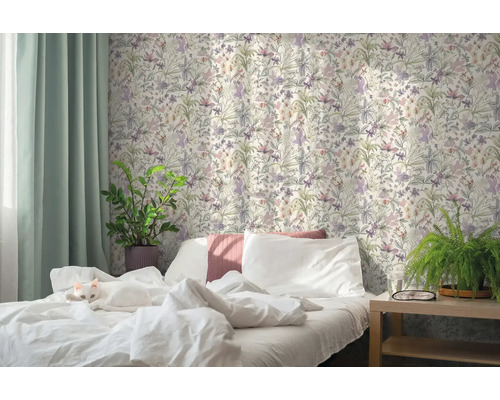 Lichte slaapkamer met een kat op het witte bed, bloemenbehang in botanische stijl, groene gordijnen en kamerplanten.