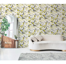 Vliesbehang met botanisch bladerpatroon in zwart en geel achter een crème bank in een lichte woonkamer.