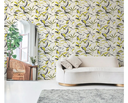 Vliesbehang met botanisch bladerpatroon in zwart en geel achter een crème bank in een lichte woonkamer.