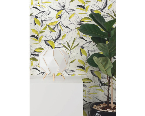 Modern vliesbehang met geel en zwart bladpatroon in schetsstijl achter een witte lamp en een groene kamerplant.