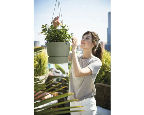 Vrouw bekijkt een hangende bloempot met witte bloemen op een balkon