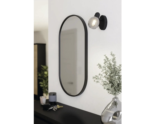 Ovale spiegel met lamp en decoratie op een dressoir.