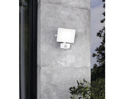 Witte buitenlamp met bewegingssensor aan een grijze muur