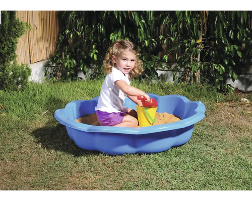Meisje speelt in een blauwe zandbak met zandspeelgoed in de tuin.
