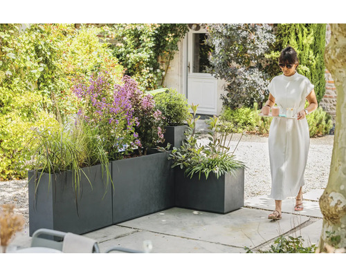 Tuinaanzicht met grijze plantenbakken en een vrouw die een dienblad draagt