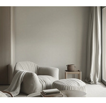 Woonkamer met fauteuil, hocker, bijzettafel en gordijnen voor een lichte en uitnodigende sfeer.