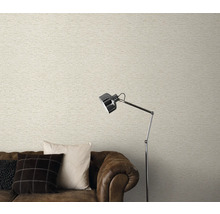 Woonkamer met licht behang in metselwerklook, bruine bank en staande lamp