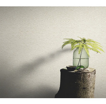 Close-up van een muur met een behang in steenlook, op een boomstronk staat een vaas met een plant.