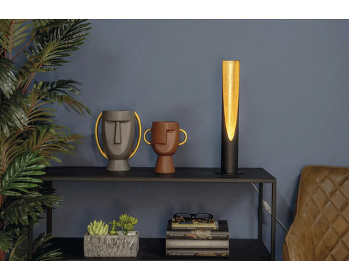 Decoratieve scène met een tafellamp, twee vazen met gezichten, kamerplanten en boeken op een plank