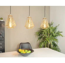 Drie goudkleurige hanglampen boven een eettafel met fruitschaal en een plant op de achtergrond.