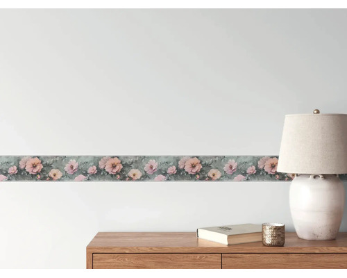 Behangrand met roze bloemenpatroon op een wand boven een houten dressoir met een tafellamp.