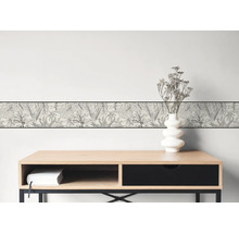Behangrand met zwart-wit botanisch bladerpatroon op een lichte muur boven een modern houten bureau.