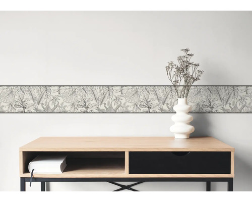 Behangrand met zwart-wit botanisch bladerpatroon op een lichte muur boven een modern houten bureau.