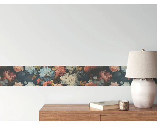 Behangrand met bloemenpatroon op een muur boven een houten dressoir met een lamp en boek.