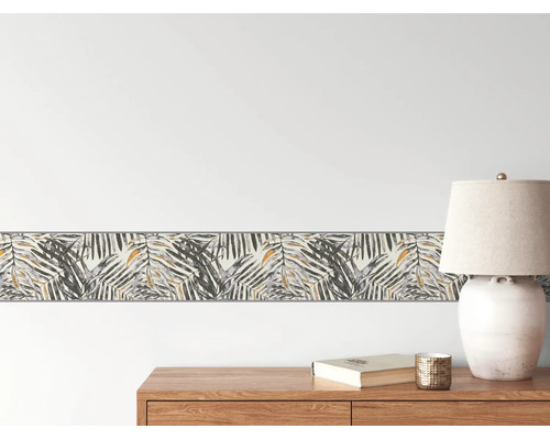 Lichte en georganiseerde scène met een behangrand in palmblad-ontwerp op de muur boven een houten dressoir met een tafellamp.